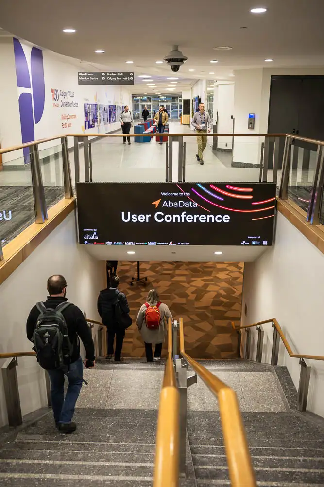 AbaData User Conference 2025 Images (1 of 20) showing a large stairwell into the conference hall at the Calgary TELUS Convention Center with a large digital billboard with modern, colourful graphics promoting the AbaData User Conference