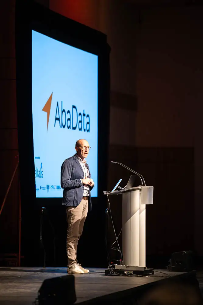 AbaData User Conference 2025 Images (3 of 20) showing our host Chris Eremenko addressing the crowd from the podium with an AbaData logo on the screen behind him